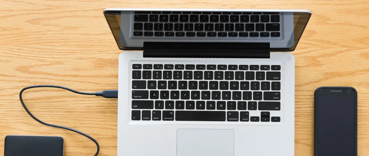 A MacBook alongside an external hard drive and smartphone.